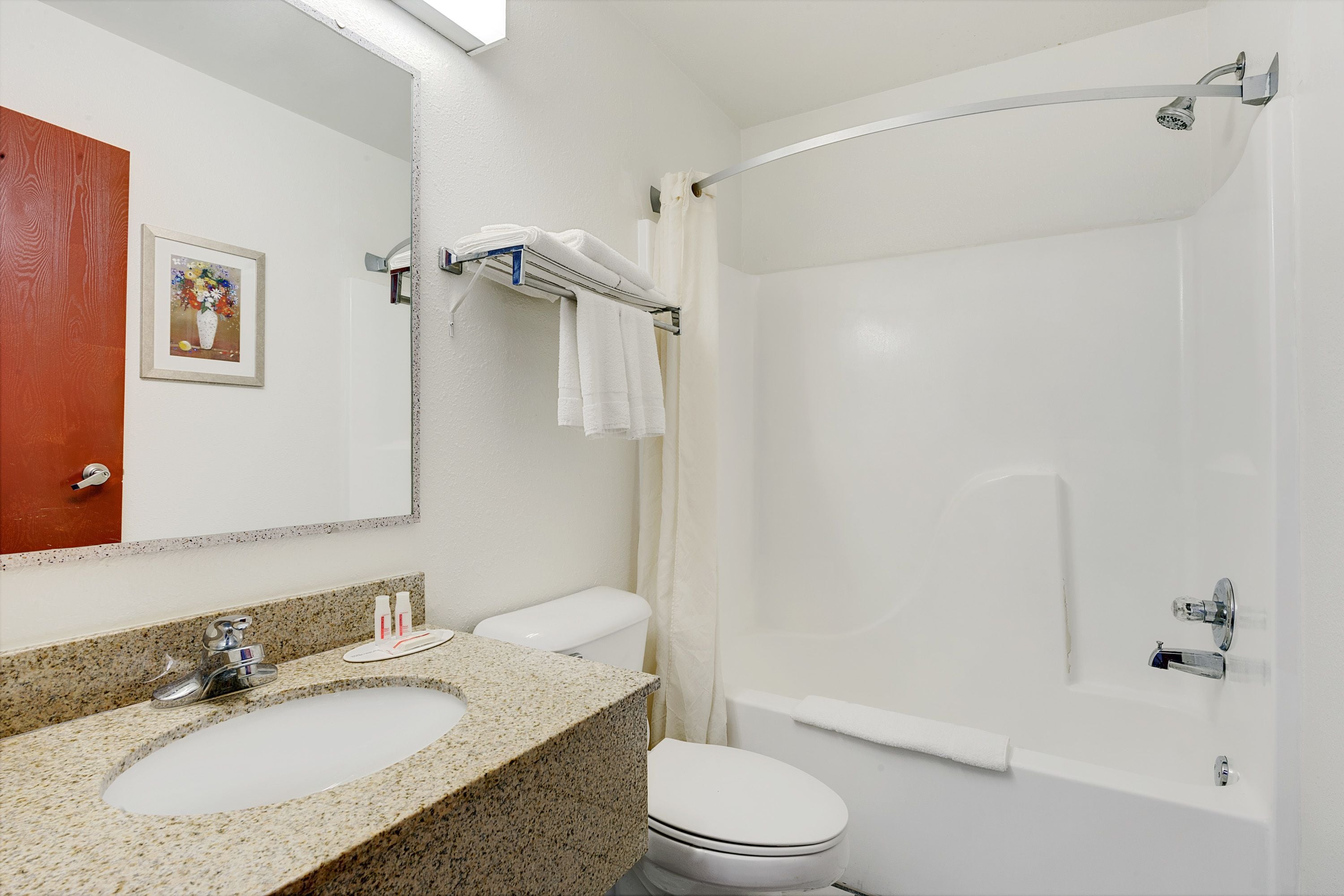 A bathroom with a granite sink, a toilet, a shower with a glass door, and a framed picture on the wall.