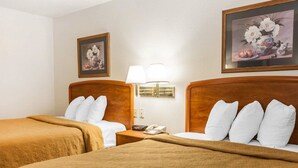 A hotel room with two beds, a nightstand with a lamp, and two framed floral paintings on the walls. - Quality Inn South (Indianapolis)
