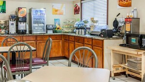 A breakfast area with a coffee machine, toaster, and waffle maker. There are wooden cabinets and a window with blinds. - Quality Inn South (Indianapolis)