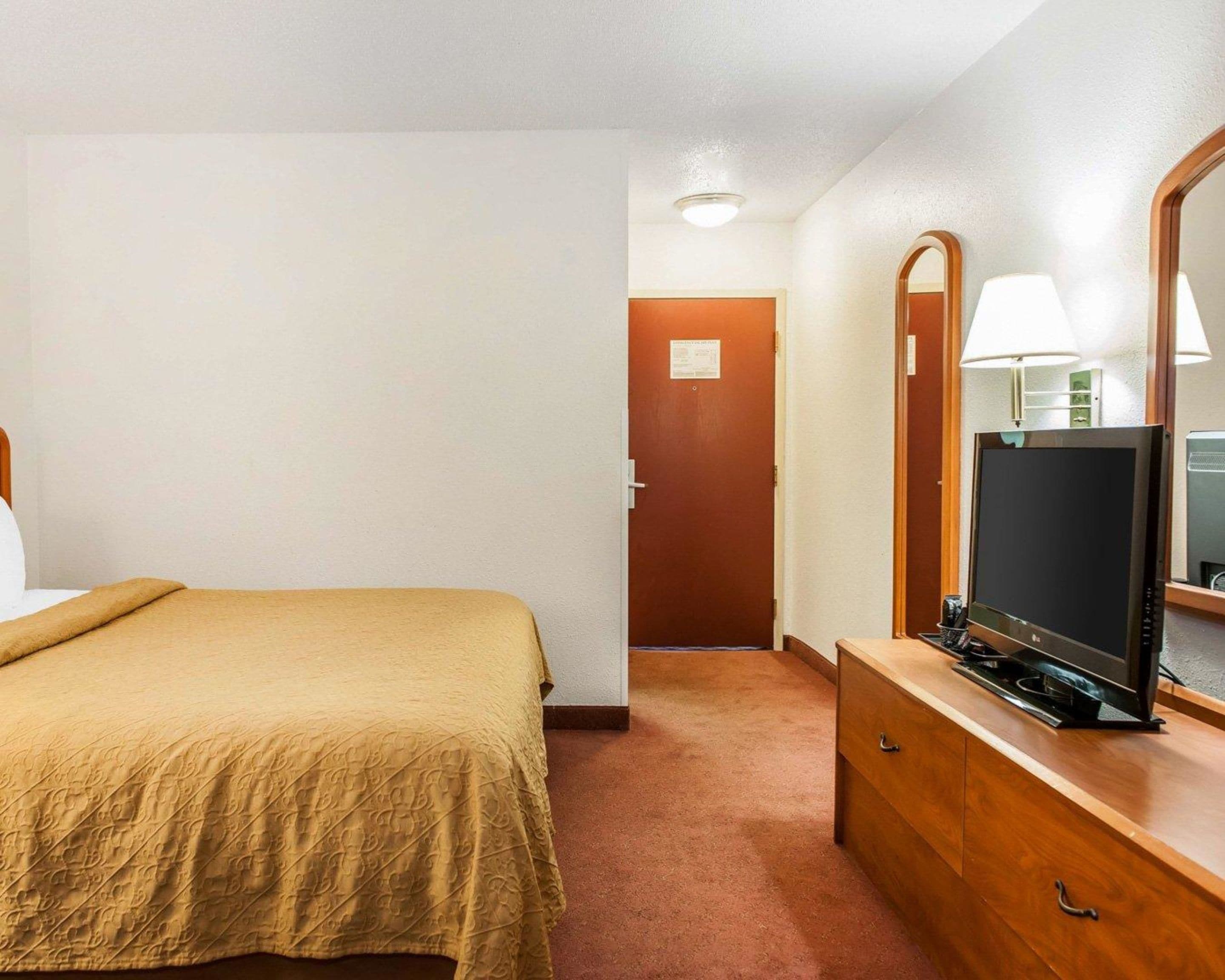 Une chambre d’hôtel comprenant un lit, une commode avec un téléviseur à écran plat, un miroir et une porte donnant sur une autre pièce.