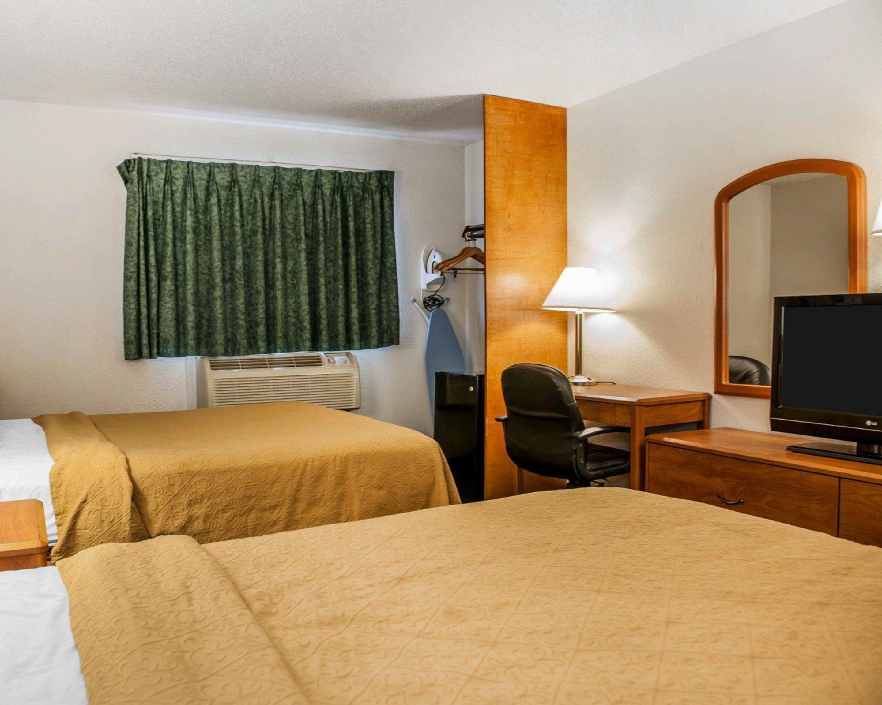 A hotel room with two beds, a desk, a chair, a television, a mirror, and a window with curtains.