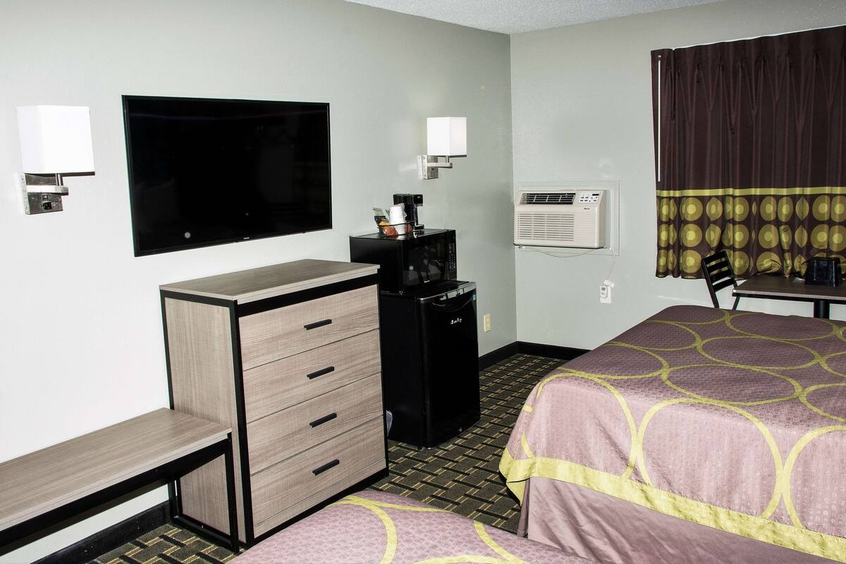 Ein Hotelzimmer mit Flachbildfernseher, Minibar, Klimaanlage und zwei Betten mit gemusterten Bettwäsche.
