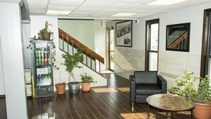 Un vestíbulo con una máquina expendedora, plantas en macetas, una escalera, un sofá de cuero negro y un suelo de baldosas.
