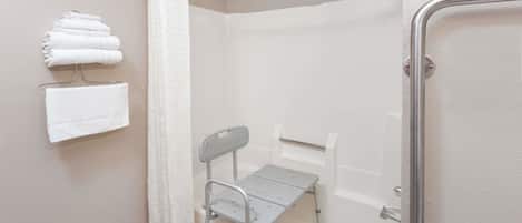 Une salle de bain avec une douche, une barre d’appui, un petit marchepied et des serviettes rangées sur un porte-serviettes.