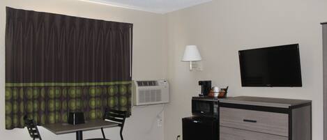 A hotel room with a bed, a desk with a chair, a television, a lamp, and a minibar.