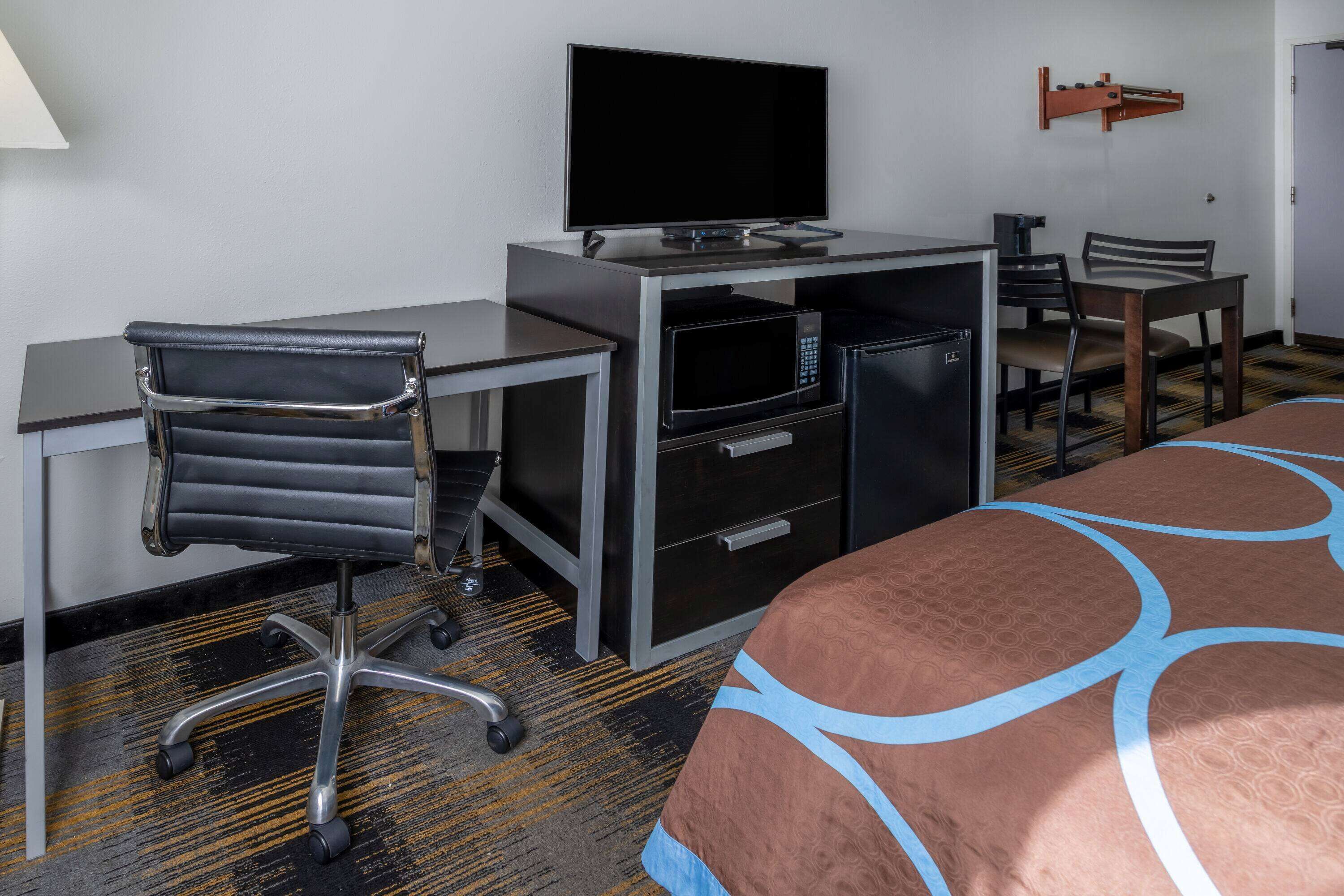 A hotel room with a bed, a desk with a computer, a television, a microwave, and a chair.