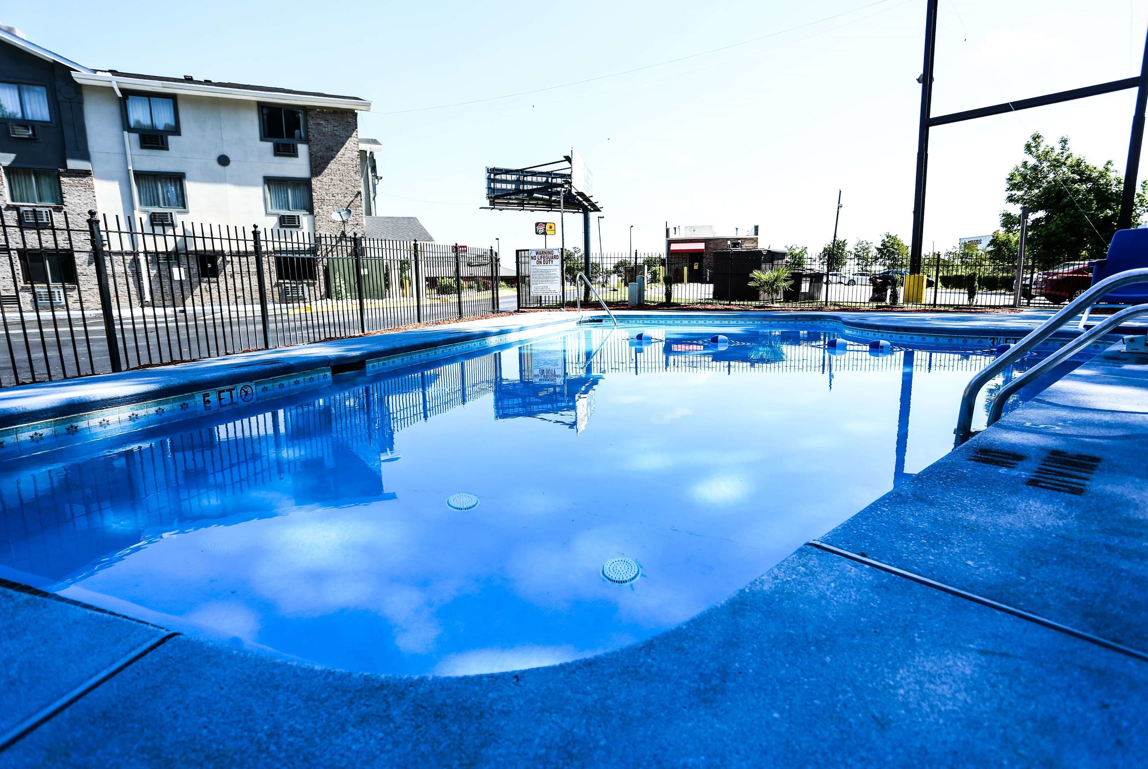 Una piscina con agua cristalina, rodeada por una valla, y edificios al fondo.