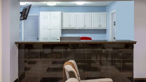 Une cuisine avec des meubles blancs, un plan de travail noir et une chaise rouge.