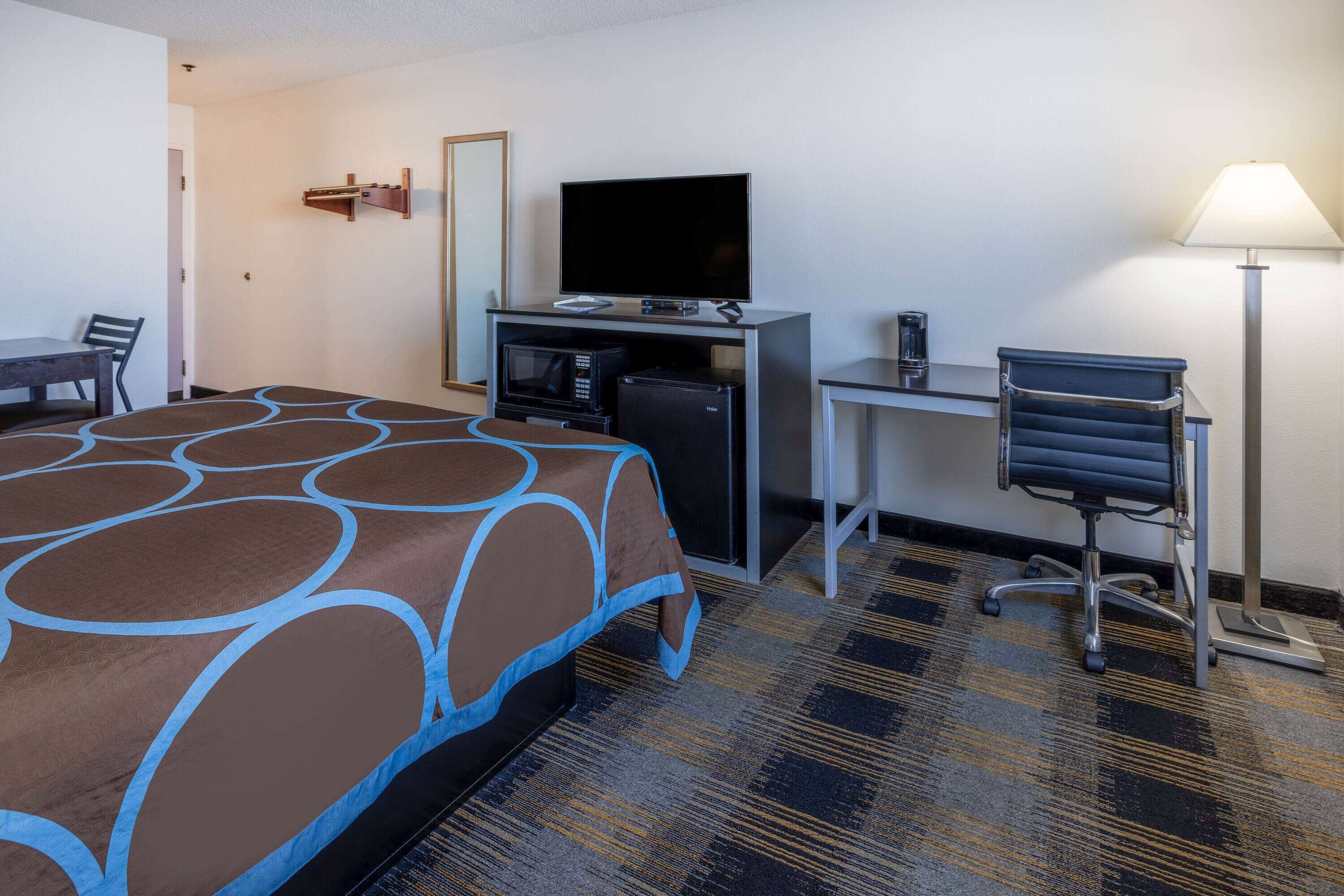 A hotel room with a bed, desk, television, microwave, and a chair.