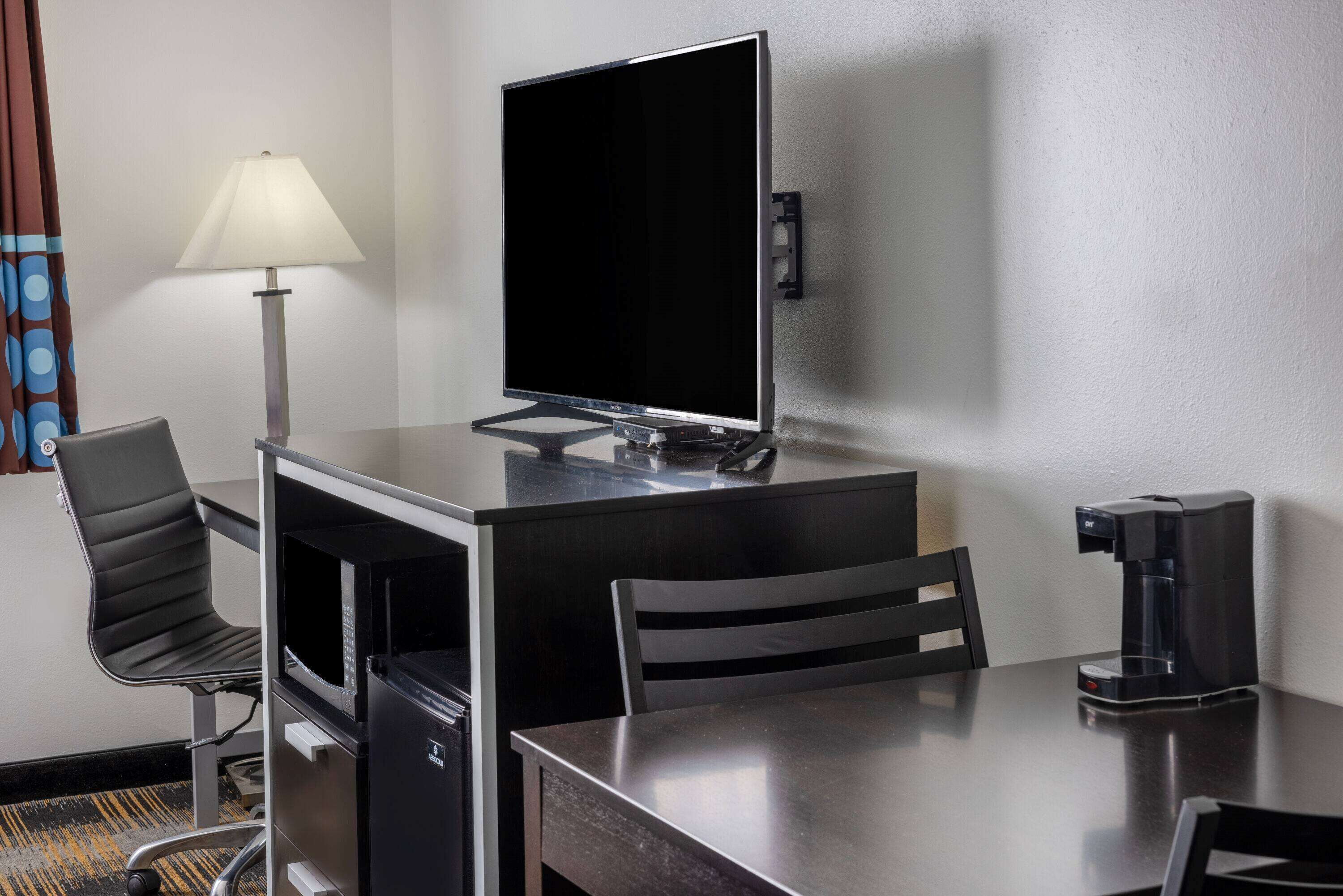 A hotel room with a desk, two chairs, a coffee maker, a TV, and a lamp.