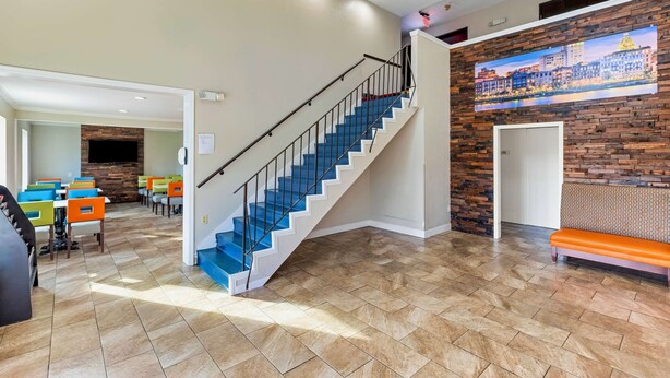 A spacious lobby with a blue staircase, a brick accent wall, and a cityscape mural. - Days Inn by Wyndham Savannah Gateway I-95 (Savannah)
