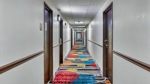 A hotel hallway with a carpeted floor, doors on both sides, and a long corridor with a ceiling light. - Days Inn by Wyndham Savannah Gateway I-95 (Savannah)