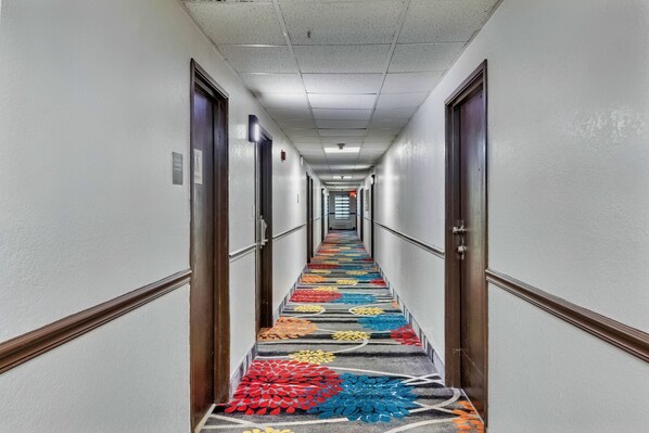 A hotel hallway with a carpeted floor, doors on both sides, and a long corridor with a ceiling light. - Days Inn by Wyndham Savannah Gateway I-95 (Savannah)
