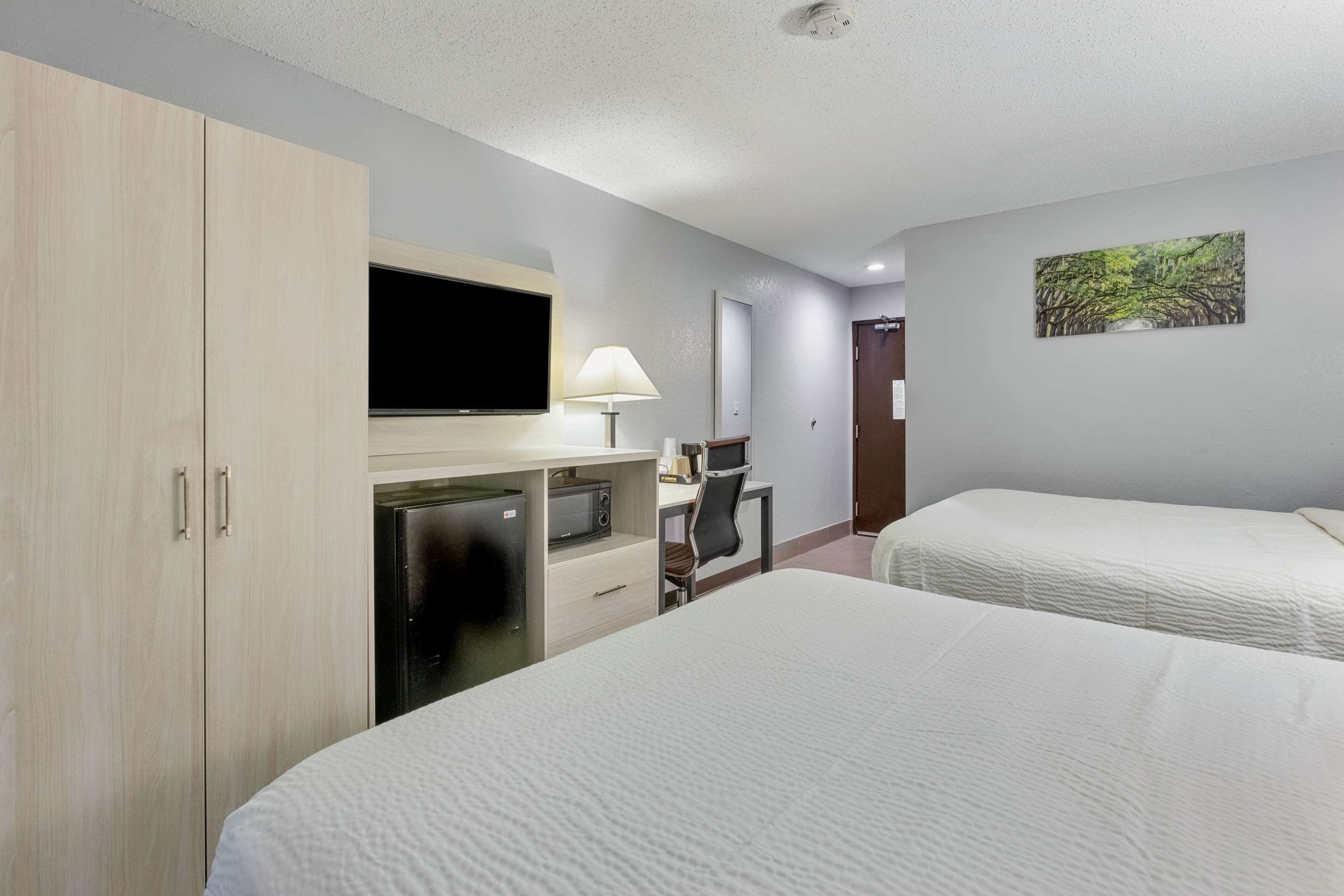 A hotel room with two beds, a desk with a computer, a TV, and a wardrobe.