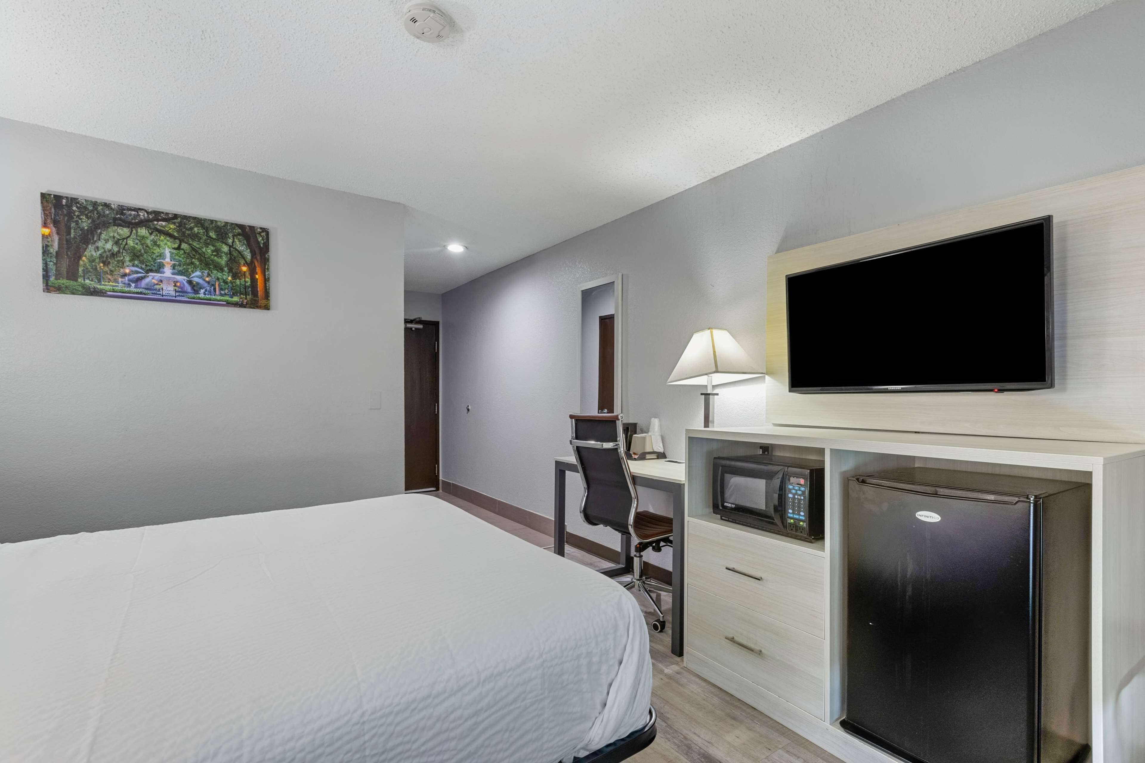 A hotel room with a bed, desk, TV, microwave, and refrigerator.
