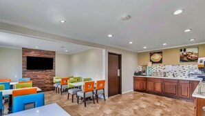 A modern dining area with multiple tables and colorful chairs, a kitchen area with a coffee station, and a flat-screen TV mounted on a wooden wall. - Days Inn by Wyndham Savannah Gateway I-95 (Savannah)