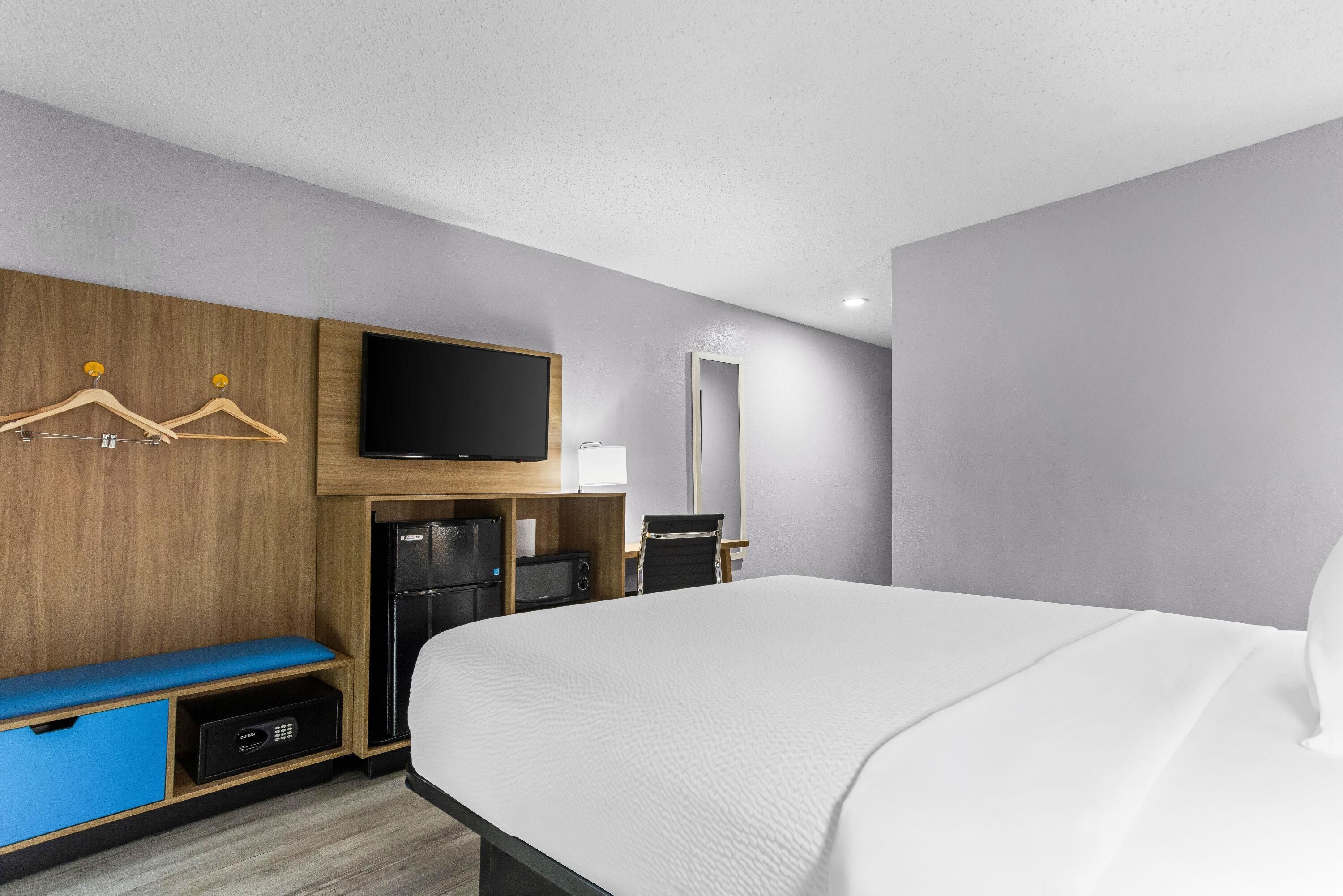 A hotel room with a bed, a television, a minibar, a desk, and a mirror.