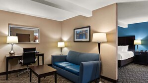 Ein Hotelzimmer mit Schreibtisch, Stuhl, Sofa und Bett. Zwei Lampen, ein gerahmtes Bild an der Wand und ein Spiegel sind vorhanden.