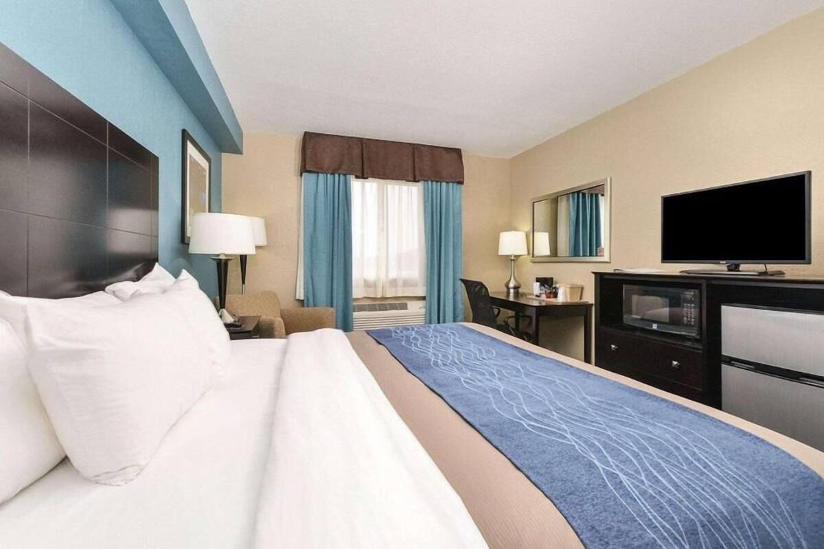 A hotel room with a large bed, a desk, a television, and a mirror.