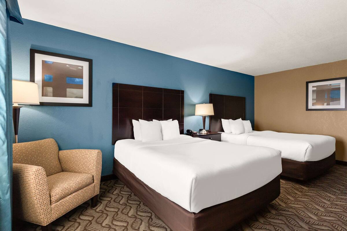 A hotel room with two beds, a sofa, and two wall-mounted lamps.