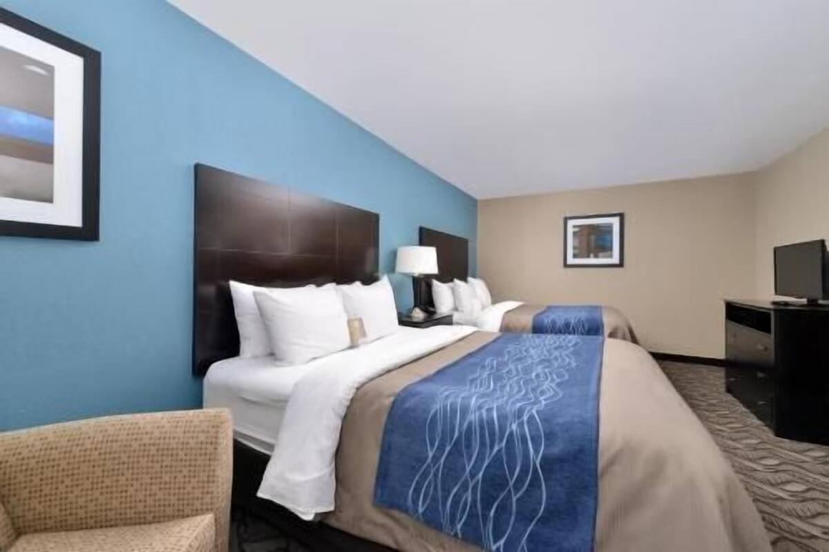 Habitación de hotel con una cama grande, una cama más pequeña, un escritorio con computadora y una silla.
