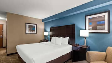 A hotel room with a large bed, a nightstand with a lamp, a chair, and a framed picture on the wall.