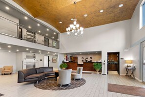 A spacious lobby with a high ceiling, a chandelier, a reception desk, and a kitchen area visible through an open door. - Comfort Inn & Suites Springfield I-55 (Springfield)