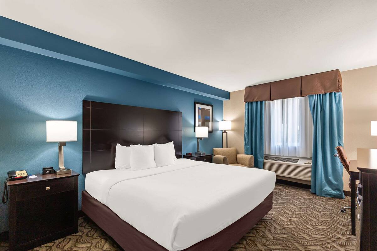 A hotel room with a large bed, two bedside tables with lamps, a chair, a desk, and a window with curtains.