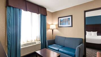 Una habitación de hotel con sofá azul, una mesita, una lámpara de pie y una cama con ropa blanca.