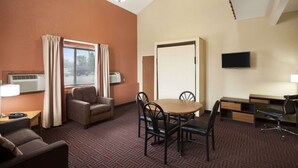 Habitación de hotel con una mesa de comedor, dos sillas, un sofá, un televisor y una ventana con cortinas.