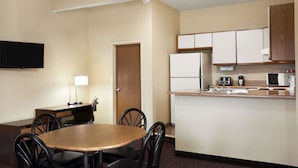 Habitación de hotel pequeña con mesa de comedor, sillas, una kitchenette y un televisor de pantalla plana en la pared.