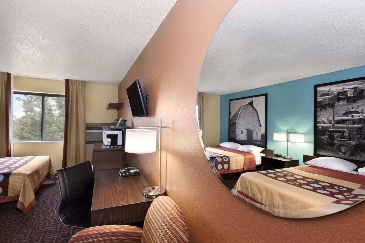 A hotel room with two beds, a desk, a chair, a TV, and a mirror.