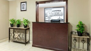 A reception desk with a framed welcome sign, two potted plants, and a decorative metal stand. - Super 8 by Wyndham Springfield East (Springfield)