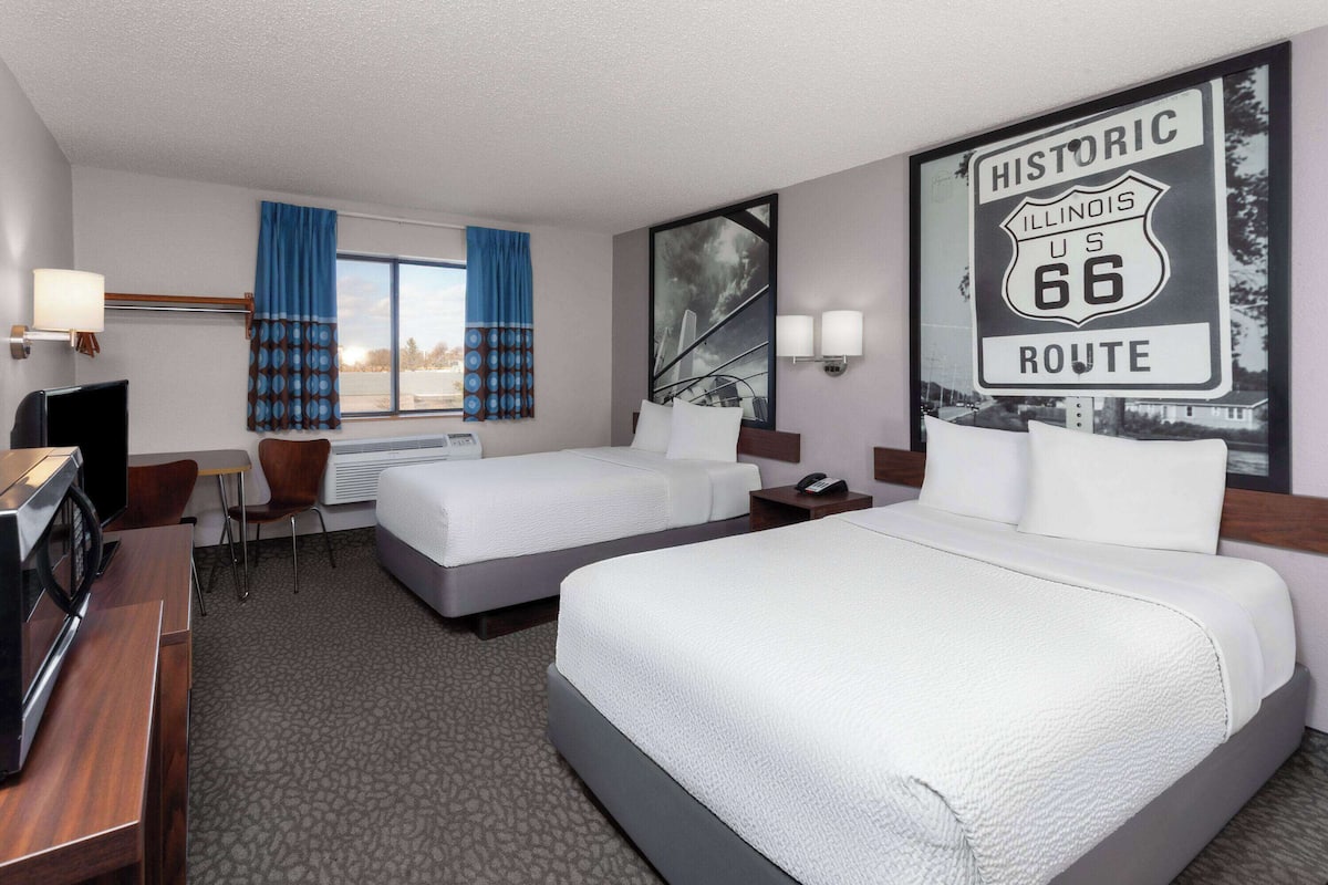 A hotel room with two beds, a desk with a computer, a chair, a TV, and a large window with curtains.