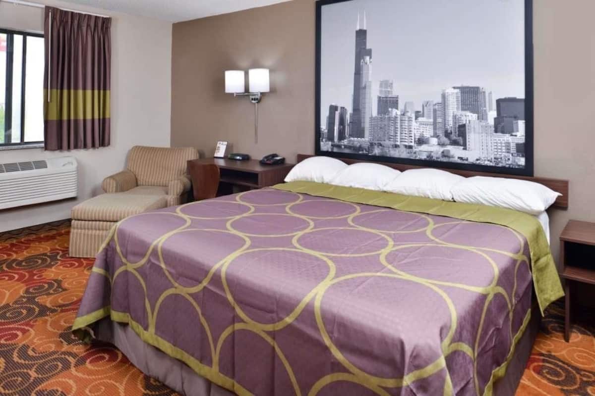 A hotel room with a bed, a chair, a desk, a cityscape view, and a window with curtains.