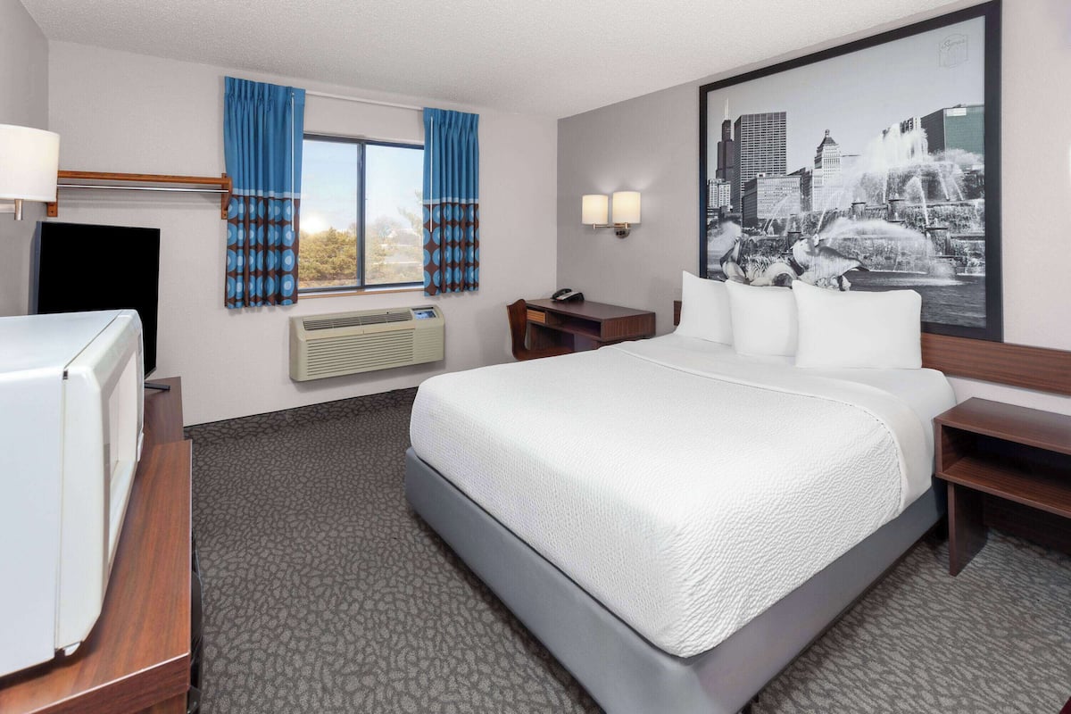 A hotel room with a bed, a desk, a chair, a TV, and a large window with curtains.