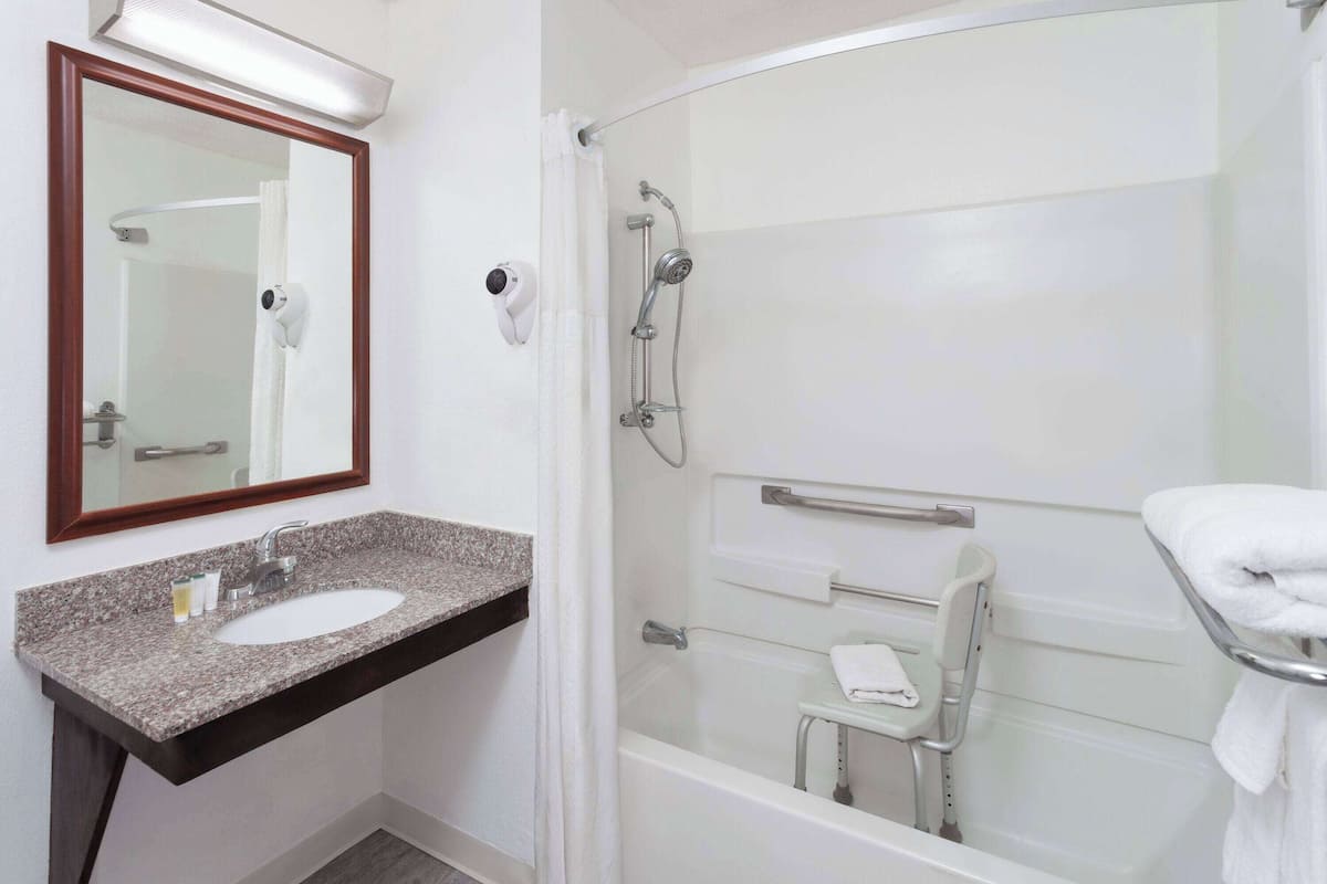 A bathroom with a granite countertop sink, a mirror, a shower with a handheld showerhead, and a grab bar.