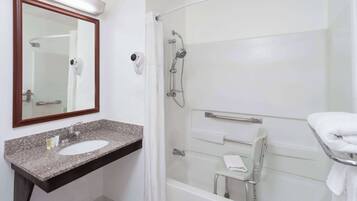 A bathroom with a granite countertop sink, a mirror, a shower with a handheld showerhead, and a grab bar.