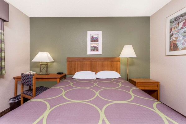 Une chambre d’hôtel avec un lit, deux tables de chevet, une chaise, une lampe et un tableau au mur.