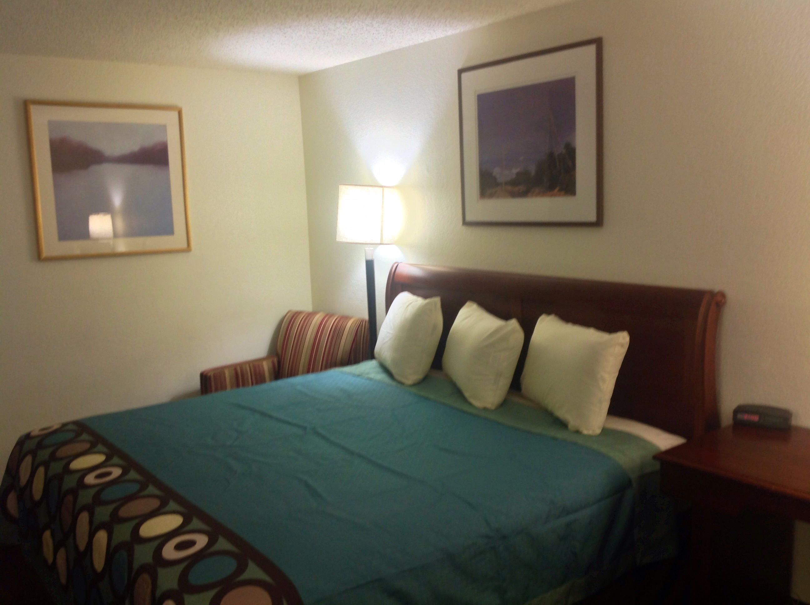 A hotel room with a bed, a nightstand, a lamp, and two framed pictures on the wall.