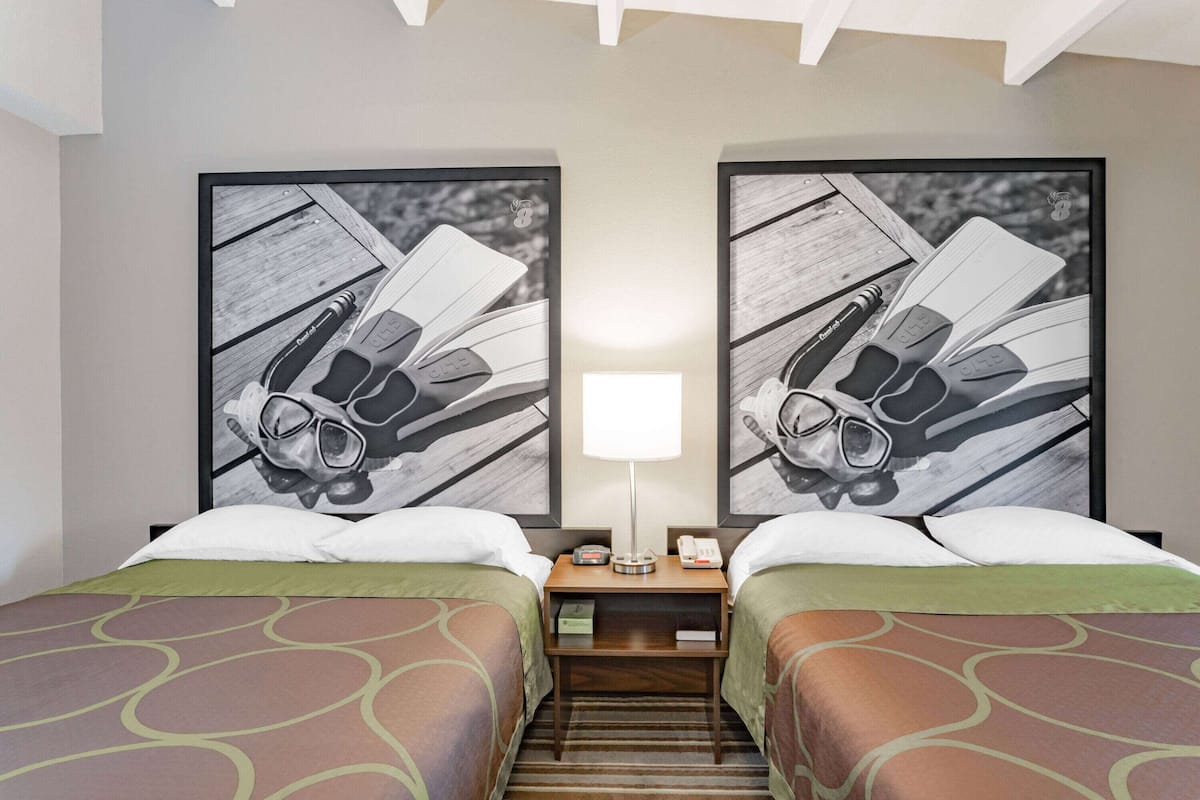A hotel room with two beds, a nightstand with a lamp, and two large framed pictures on the wall.