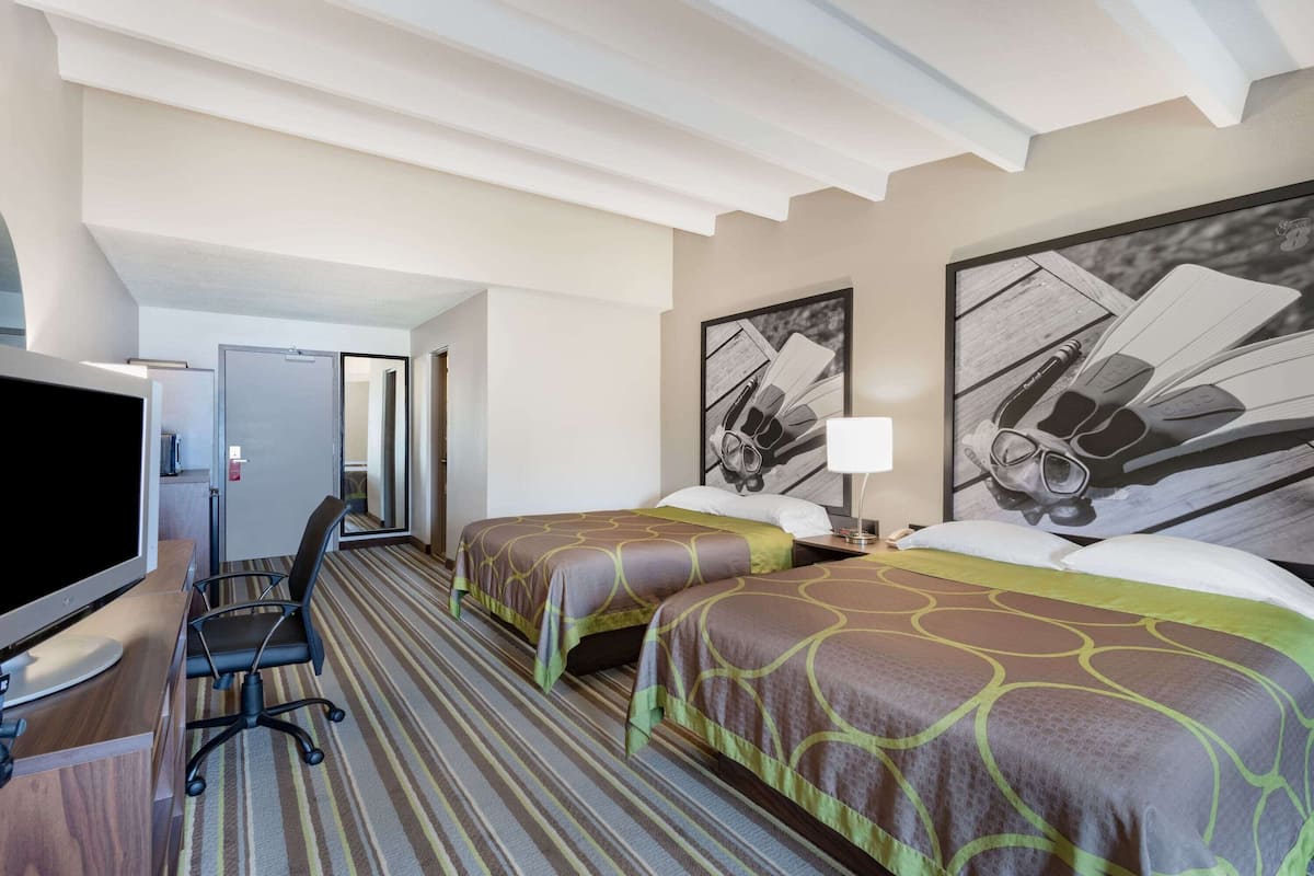 A hotel room with two beds, a desk with a computer, a TV, and artwork on the walls.