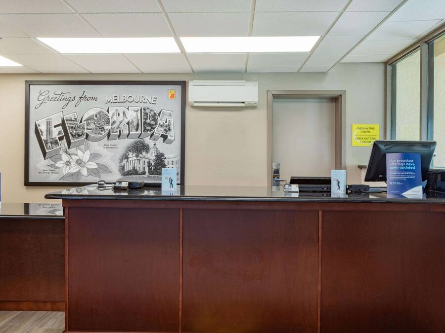 A reception desk with a framed welcome sign, a computer monitor, and a check-in kiosk.