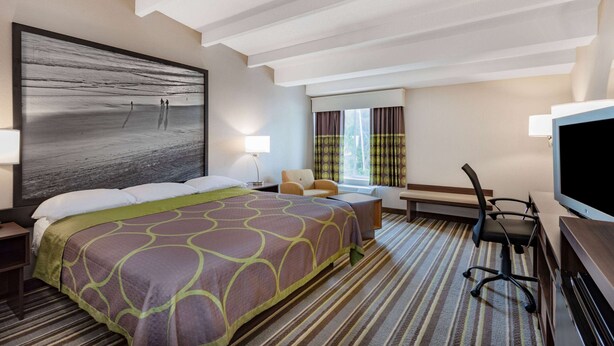 Une chambre d’hôtel avec un grand lit, un bureau avec une chaise, une télévision et une fenêtre avec des rideaux.