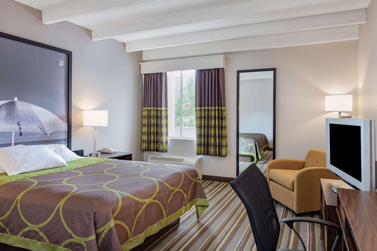A hotel room with a large bed, a desk with a TV, a chair, a desk lamp, and a window with curtains.