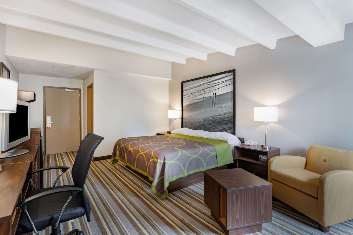 A hotel room with a bed, a desk with a computer, a chair, a sofa, and a painting on the wall.