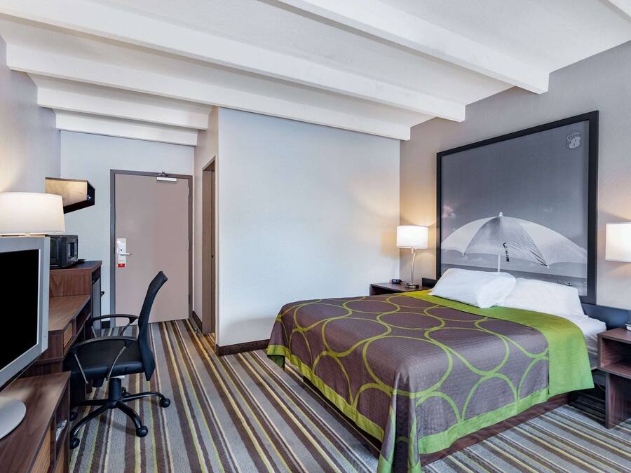 A hotel room with a bed, a desk with a computer, a chair, and a TV.