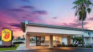 Un motel de type Super 8 doté d’un parking couvert, de palmiers et offrant une vue sur un ciel au coucher du soleil.