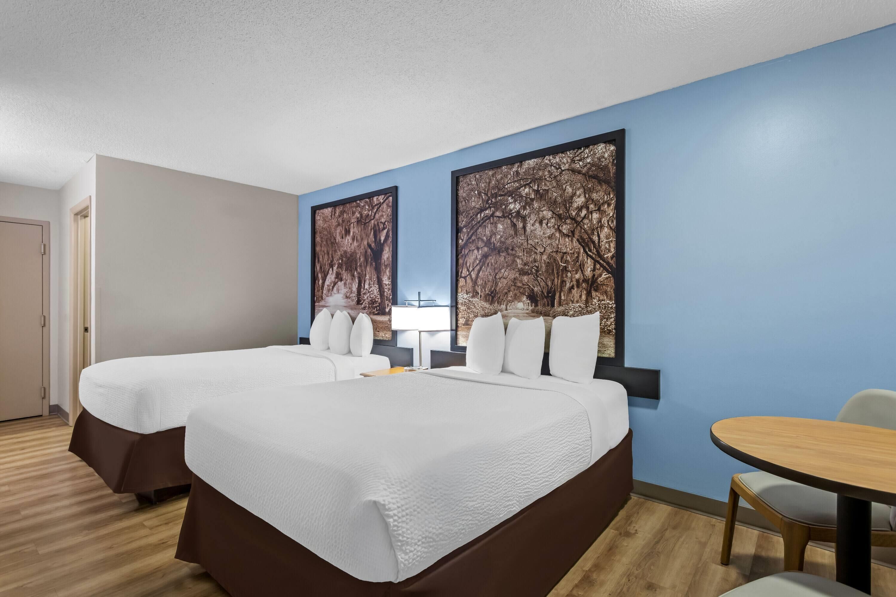 Une chambre d’hôtel avec deux lits, une table ronde et deux grandes œuvres d’art mural.