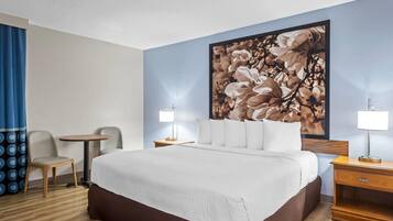 A hotel room with a large bed, two bedside tables, a small round table, a chair, and a large floral artwork on the wall.